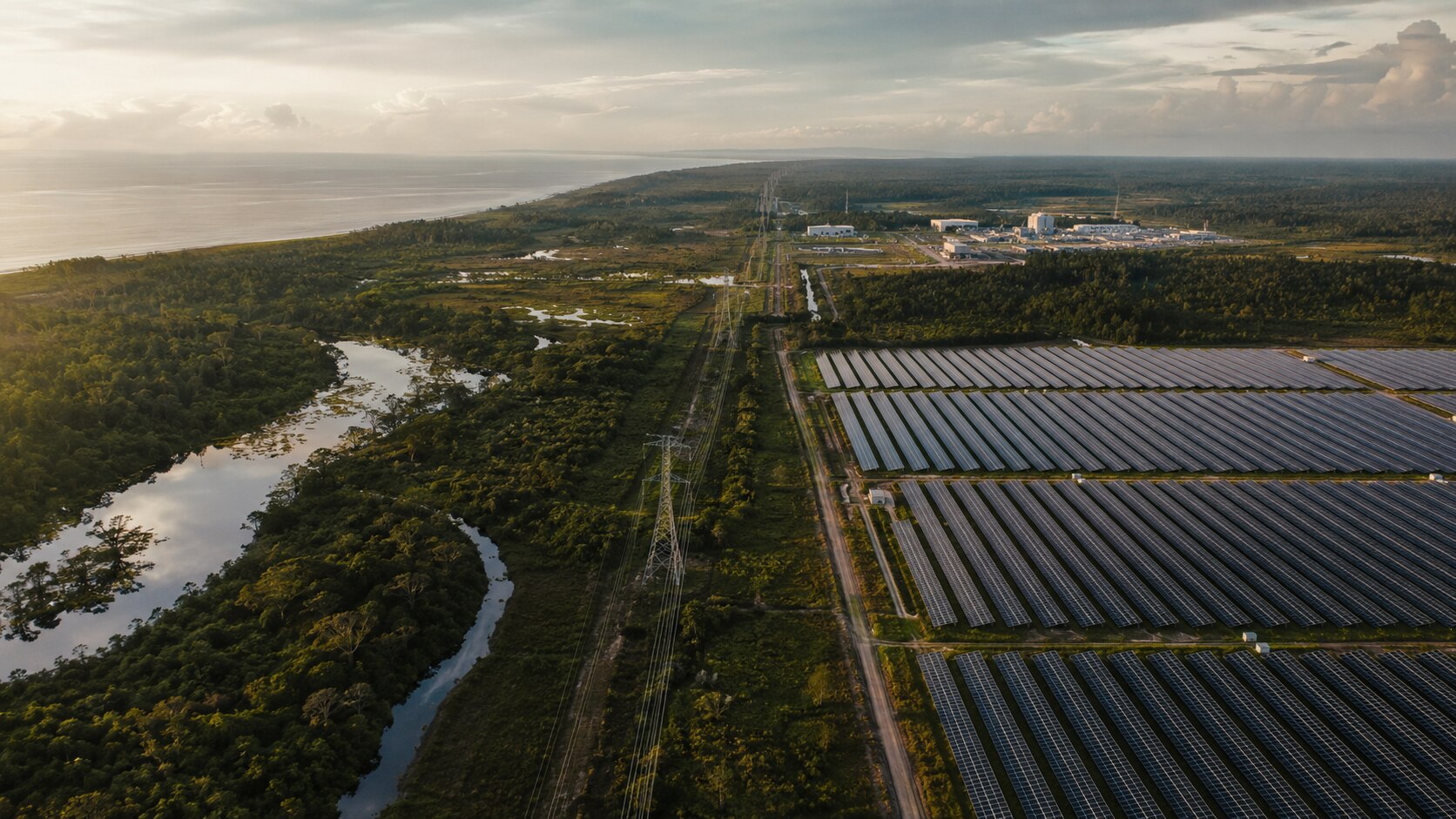 Aerial view of a coastal landscape with transmission corridors and a large solar array beside forest and waterways.