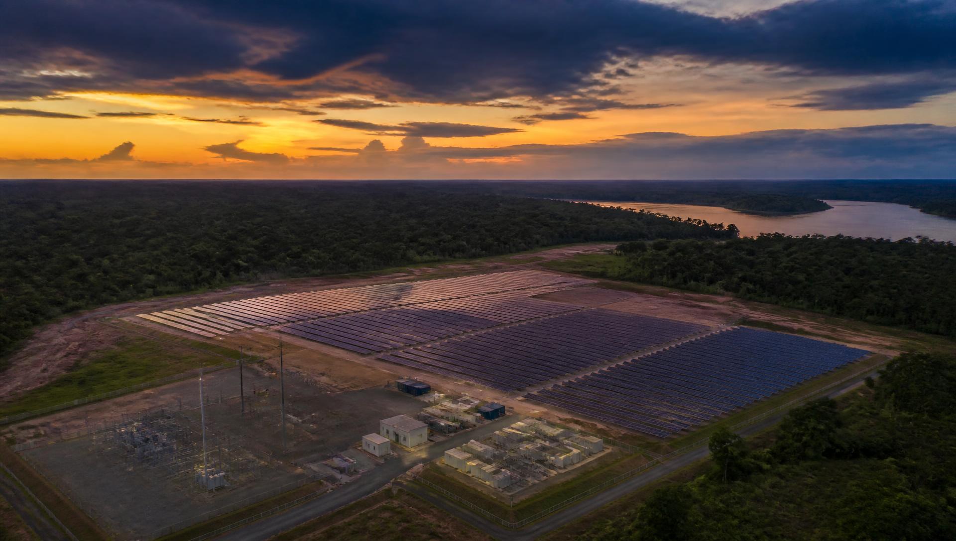Aerial view at dusk of a utility-scale solar array beside rainforest and a river.